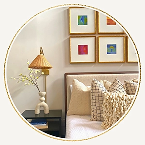 Circular graphic frame showcasing a detailed bedroom corner featuring a black nightstand with a woven wicker wall sconce, plaid accent pillows, and a colorful grid gallery wall
