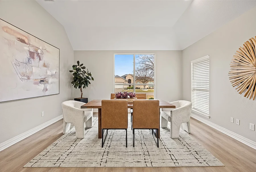 Staged transitional dining room with a long wood table, two camel leather chairs, four white textured accent chairs, and a large abstract canvas painting on a light neutral wall