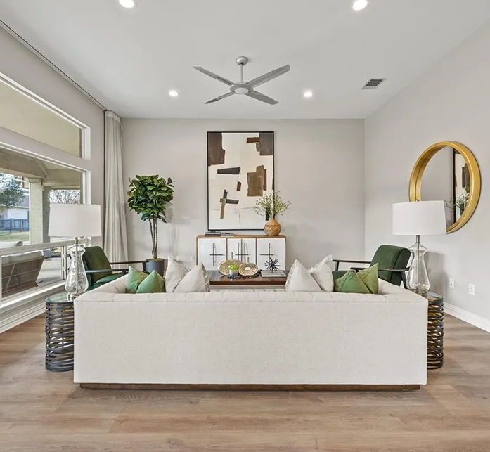 Staged formal living area looking straight at a beige sofa flanked by two forest green velvet armchairs, wire-frame side tables, and a large black-and-white graphic art piece