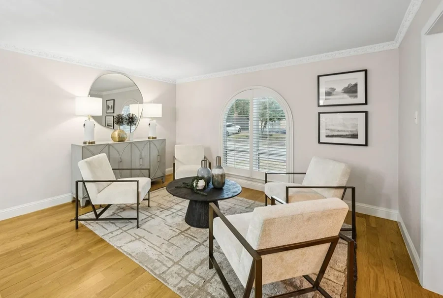 Staged formal sitting room featuring four cream armchairs around a black wooden coffee table near an arched window with shutters