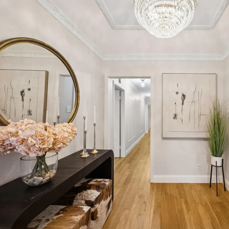 Entryway hall staging with a dark wood console table, round gold mirror, patterned stools, and a crystal chandelier
