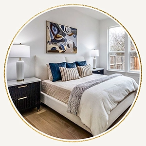 Staged bedroom with a cream upholstered bed, blue and striped accent pillows, dark wood nightstands, and abstract wall art