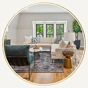 Sunlit living area showcasing a cream sectional sofa, a teal accent armchair, a patterned rug, and a gold side table