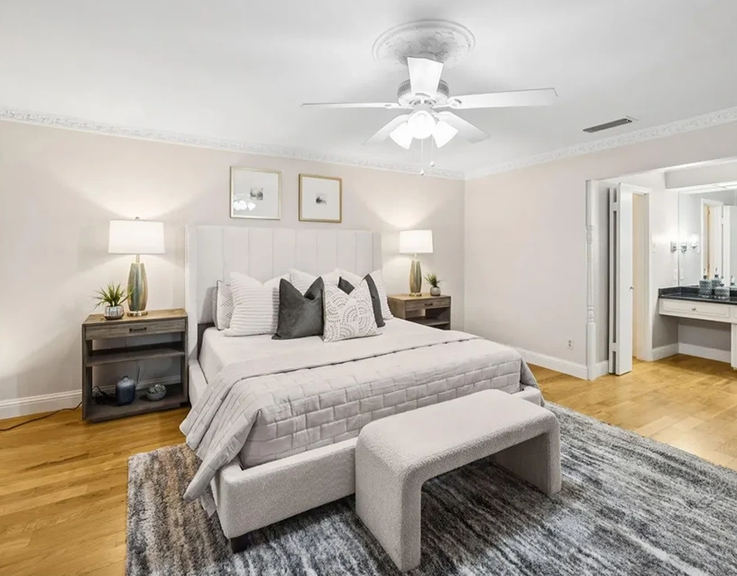 Staged primary bedroom with a vertical channel-tufted headboard, white bedding, and a bouclé bench
