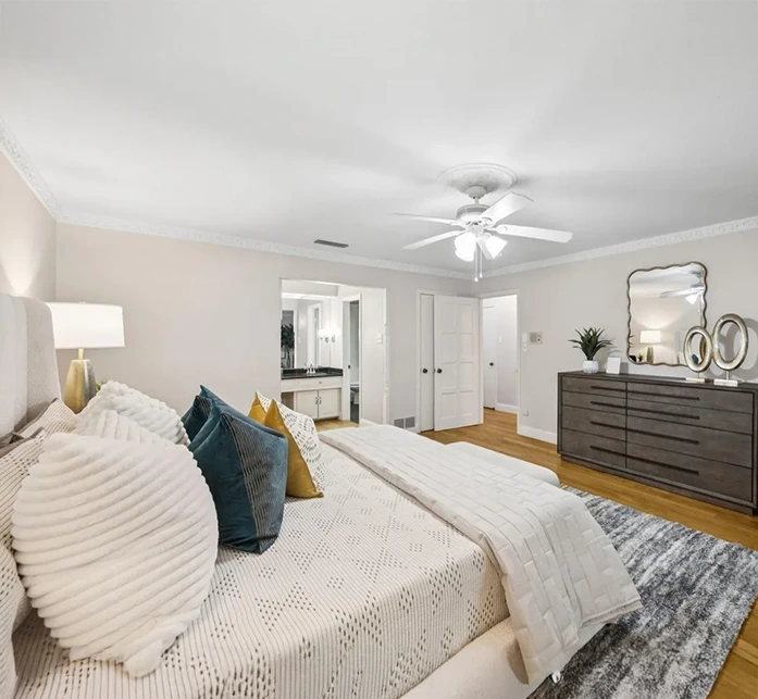 Staged bedroom vignette showing a dark wood dresser, silver mirror, and textured blue accent pillows