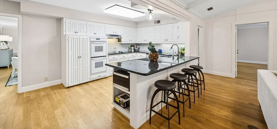 Staged kitchen featuring white geometric panel cabinets, dark granite countertops, and a breakfast bar with stools