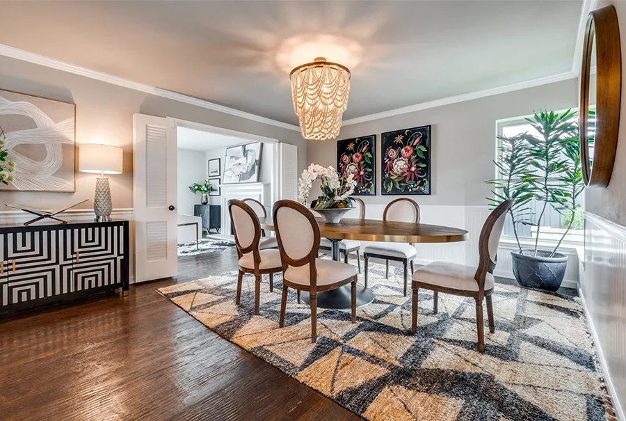 Staged formal dining room featuring an oval wooden table, a tiered beaded chandelier, and a geometric black-and-white buffet cabinet