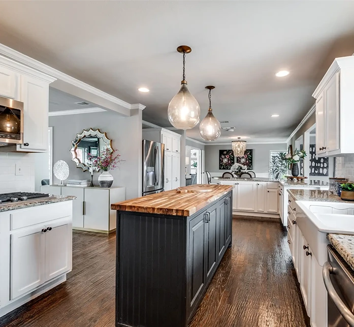 Kitchen view highlighting a long black kitchen island with a butcher block countertop and teardrop glass pendant lights