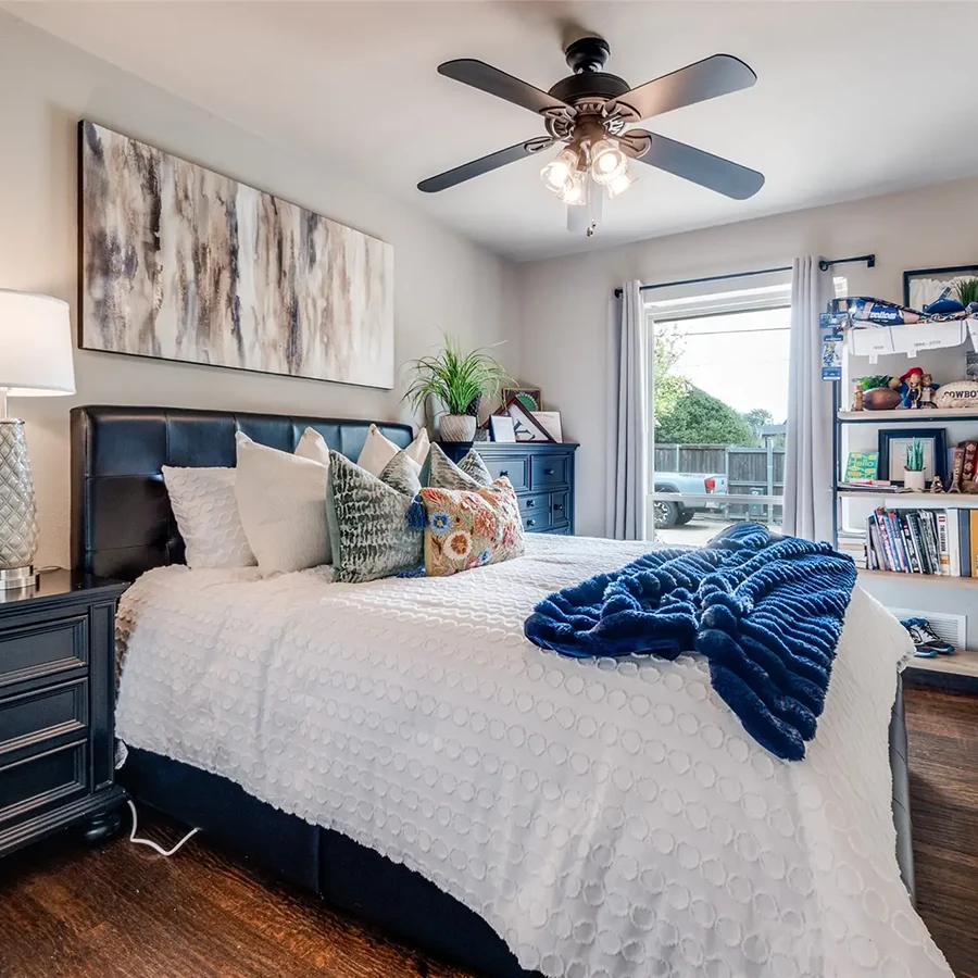 Staged bedroom featuring a black leather headboard, a white textured duvet, and a vibrant dark blue throw blanket