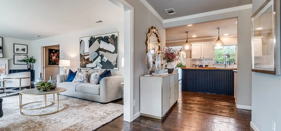 Open view from an entryway showing a cream console table under a wavy gold mirror, leading into a staged living room