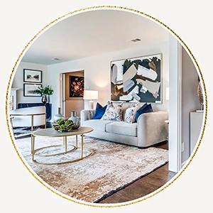Circular vignette of a staged living area with a neutral sofa, blue accent pillows, gold nesting coffee tables, and a large abstract painting