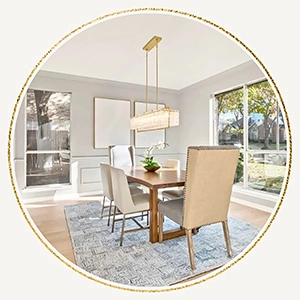 Circular vignette of a bright dining space featuring a long wooden table, high-back upholstered chairs, and a modern rectangular chandelier