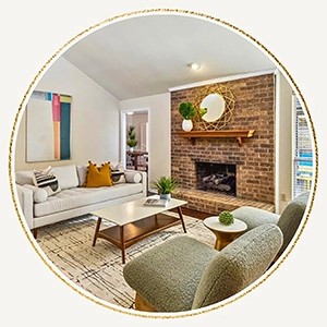 Circular vignette of a staged mid-century living room featuring a brick fireplace, a white sofa with mustard yellow pillows, and green armchairs