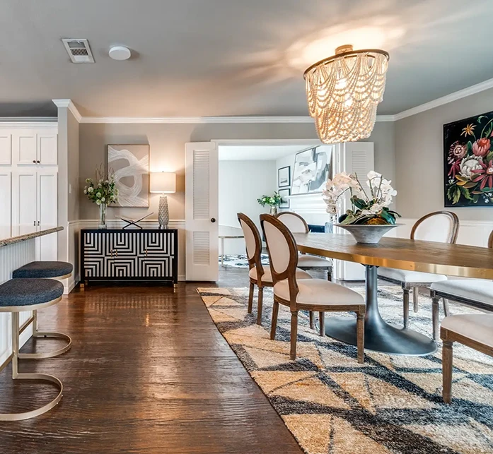 Staged dining room featuring a long wooden table, white upholstered chairs, and a statement beaded chandelier