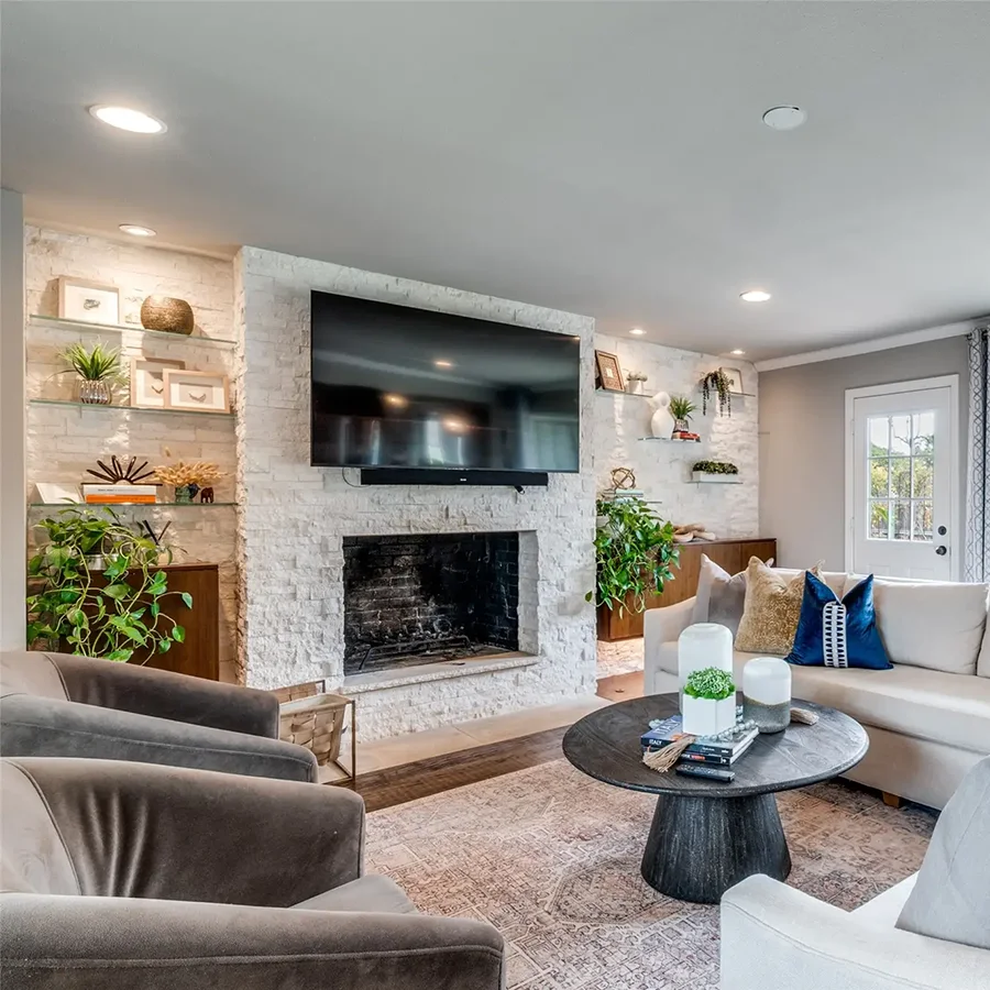 Living area staging highlighting a white stacked stone fireplace wall with a mounted TV and built-in glass shelves with greenery and decor