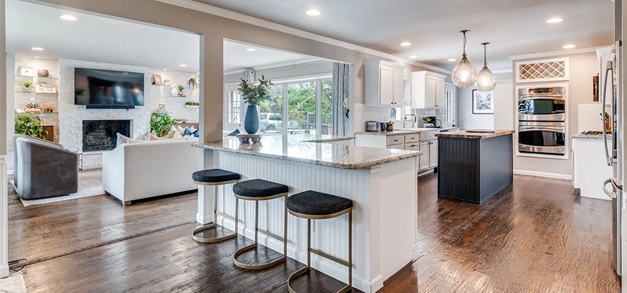 Open-concept staged kitchen with a white breakfast bar, black stools, granite countertops, and a dark island