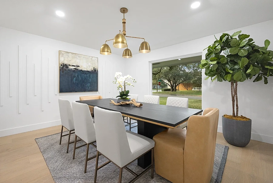 A sleek black dining table paired with six white quilted chairs and two cognac leather captain's chairs, positioned under a modern brass chandelier with a large green fiddle-leaf fig tree in the corner.