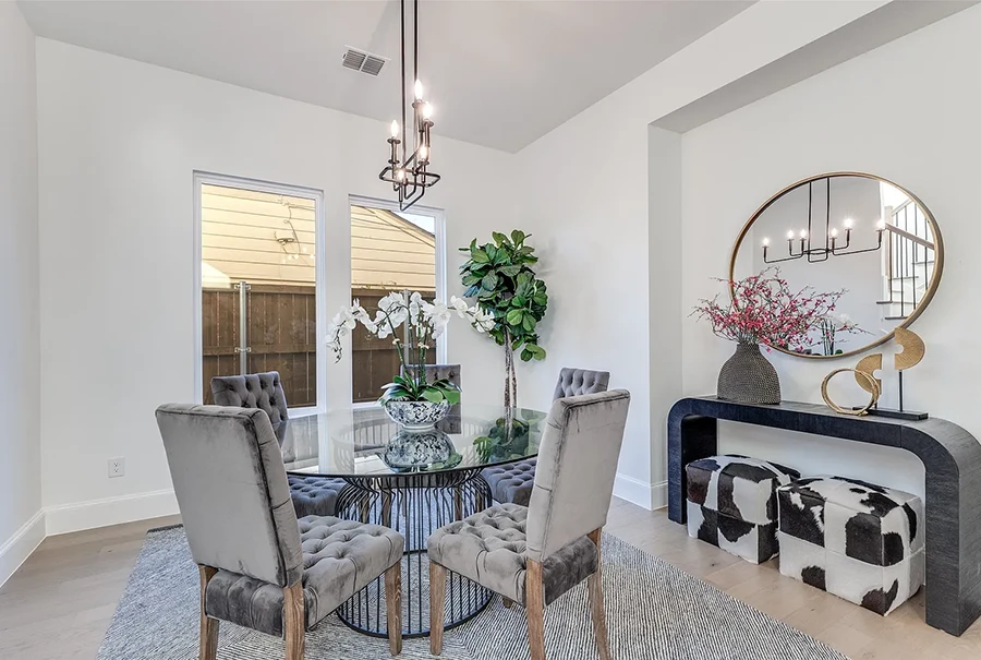 Dining room staged with a large round glass table, five upholstered high back chairs, black console tabel and two rawhide ottomans