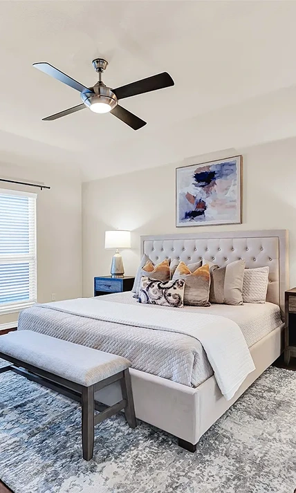 Bedroom staged with a light grey upholstered bed, grey bench and lots of pillows
