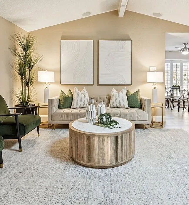 Media room staged with a light tan sofa, green pillows, green accent chair and round wooden coffee table