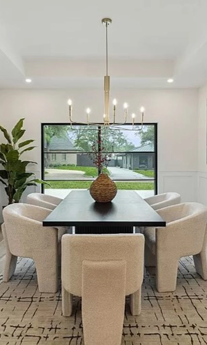 Dining room staged with large rectangular dark wood table, six modern white upholstered chairs and large white and black rug