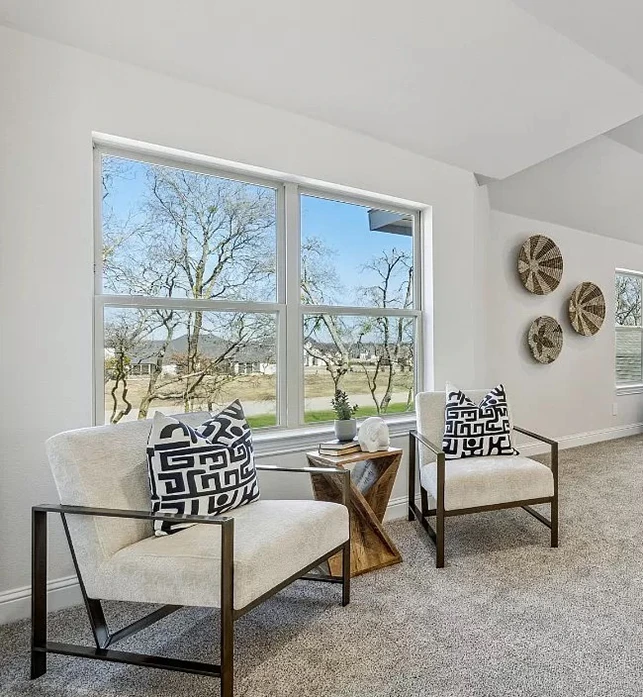 Seating area staged with two white chairs with metal frames, abstract black and white pillows and a small accent table