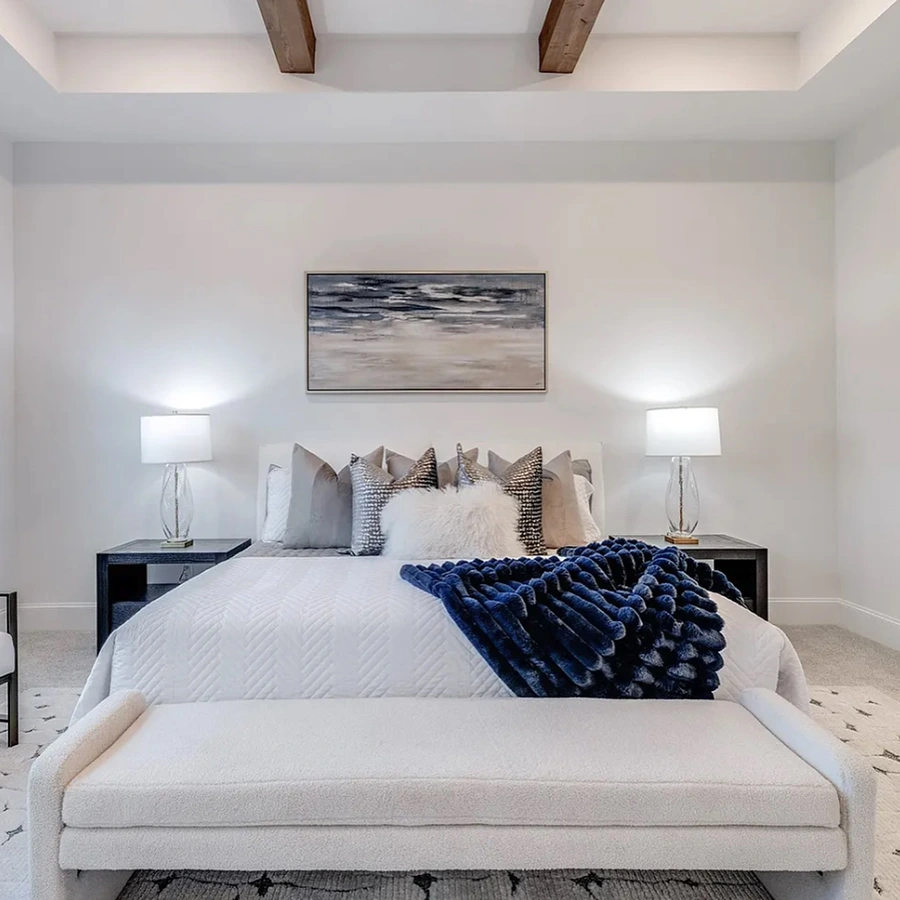 Staged bedroom room with white upholstered bed, white upholstered bench, blue throw and grey pillows