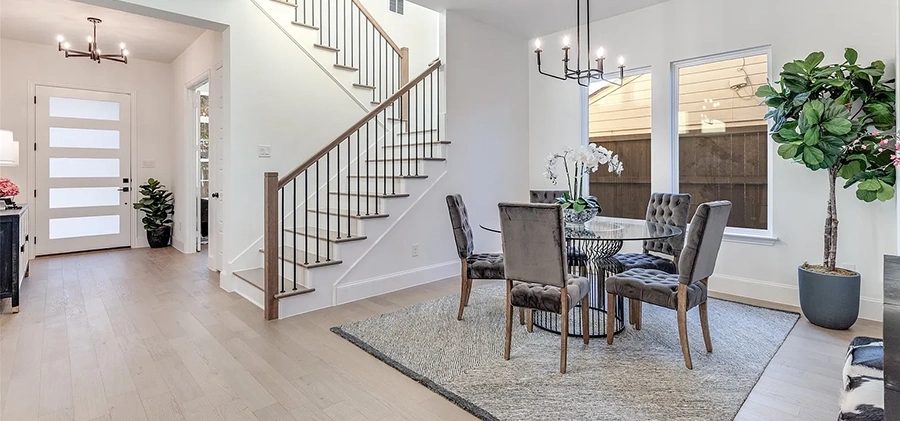 Large entryway staged with console table and mirror, dining area with round glass table and five grey upholstered chairs