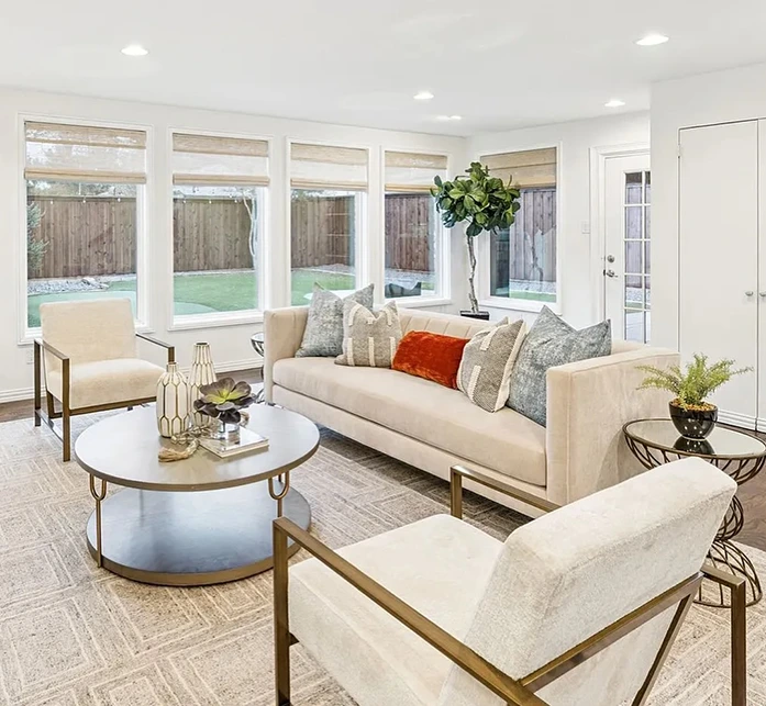 Modern living area staging with a white sofa and two white chairs that are gold-framed and a round matching coffee table