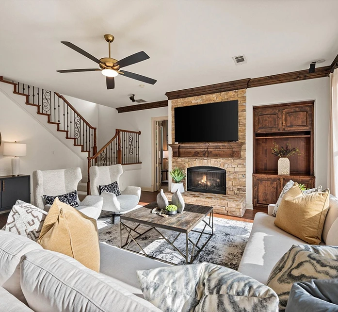 Wide view of living area with an l-shaped sofa, two white barrel chairs facing a fireplace