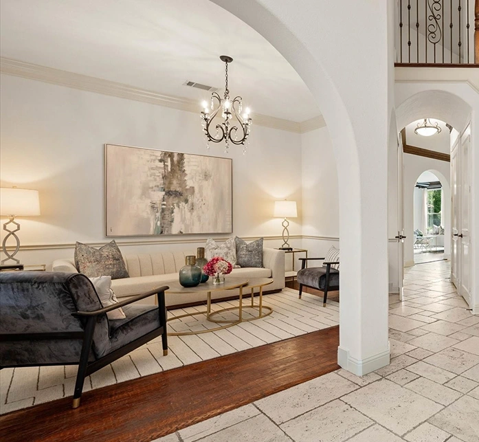A view looking through a white archway into a sitting area that features a light beige sofa, a gold tiered coffee table, and a large abstract painting in muted tones.