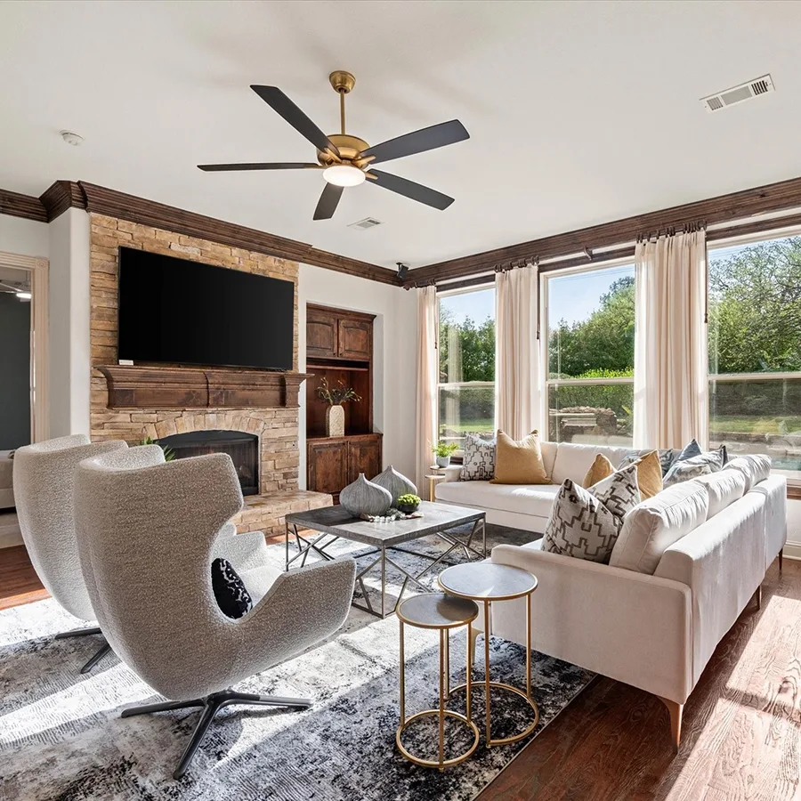 A wide-angle view of the main living area, showing the relationship between the stone fireplace, the white sectional sofa, and the high-back accent chairs under a dark wood beamed ceiling.