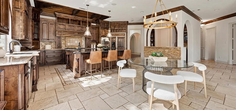 A comprehensive view of the open-concept kitchen and breakfast area, highlighting the dark wood island with cognac leather barstools, the stone-accented walls, and the glass dining table.