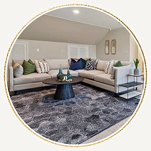 Living area staged with an l-shaped sofa, round black coffee table and colorful pillows