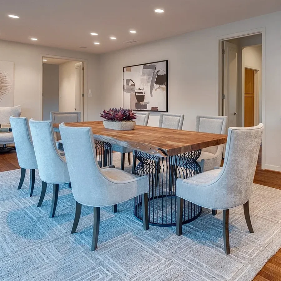 Dining room staged with a large rectangular wood table with a metal base, eight high back grey chairs and large abstract artwork