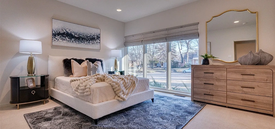 Bedroom staged with a white upholstered bed, black nightstands, cream and blue pillows, and large blue, grey and white rug