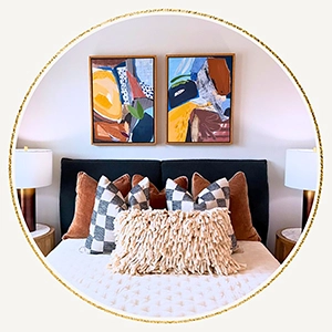 Close up of a staged bed with a black upholstered headboard, tan pillows, and colorful abstract artwork