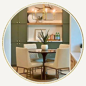 Small dining area staged with a round metal table, four beige leather chairs and a white vase with greenery