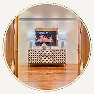Entryway staged with a large white and wooden console table, large rectangular gold framed mirror, two white lamps and large vase with flowers