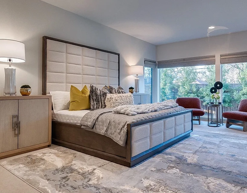 Bedroom staged with a very large grey and dark wood upholstered bed, grey and white bedding, two rust colored side chairs and large nightstands