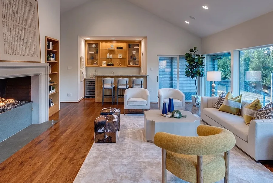 Living area staged with a white sofa, yellow boucle chair, a modern large coffee table, two rawhide ottomans