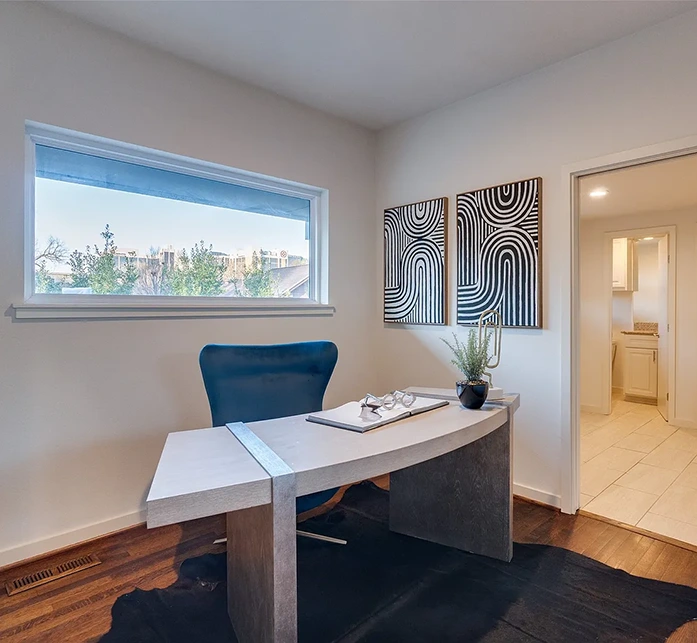 Office staged with a modern grey desk, a large blue desk chair, rawhide rug and blue and white artwork