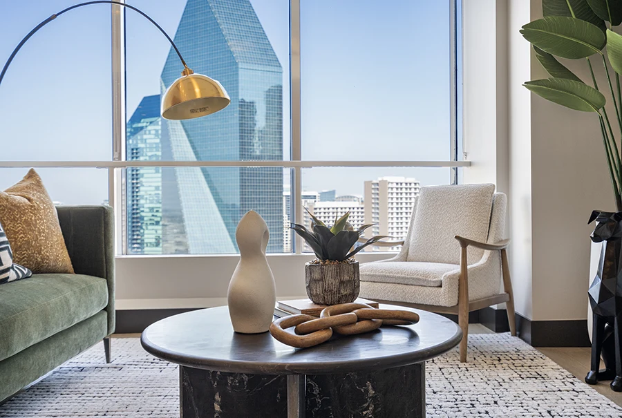Close-up of modern living room staging featuring a dark marble coffee table, a white textured armchair, and a large window overlooking the Dallas skyline