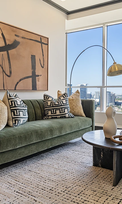 Stylish living area showcasing a green velvet sofa with patterned pillows, abstract wall art, and a gold arched floor lamp near a high-rise window