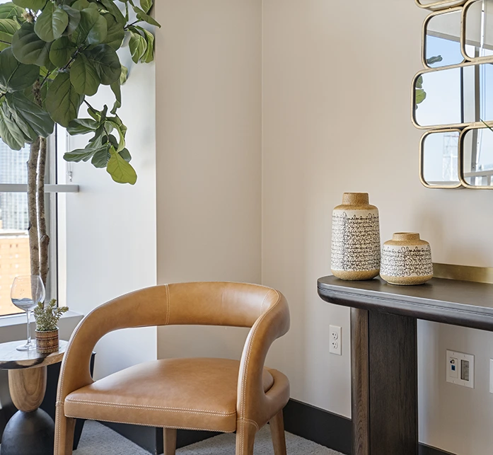 A curated seating nook with a tan leather chair, a fiddle leaf fig tree, and decorative vases on a dark wood console table