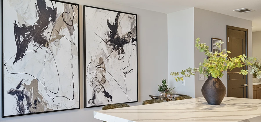 Large abstract black and white canvas paintings displayed on a light gray wall behind a white marble kitchen island with a decorative vase
