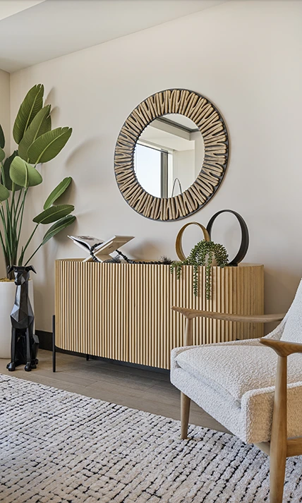 Modern home staging featuring a light wood fluted sideboard, a decorative round sunburst mirror, and a sleek white boucle armchair