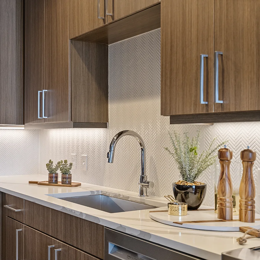 Detailed view of a modern kitchen staging with a stainless steel sink, white herringbone tile backsplash, and wooden kitchen accessories on a marble countertop