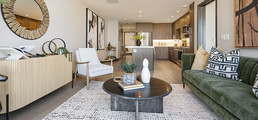 Open-concept living and kitchen area in a Dallas high-rise, featuring a green velvet sofa, white armchair, and large abstract wall art