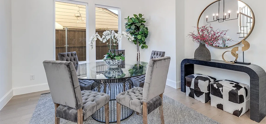 Staged dining room with round table, four velvet chairs, black console table and two rawhide ottomans